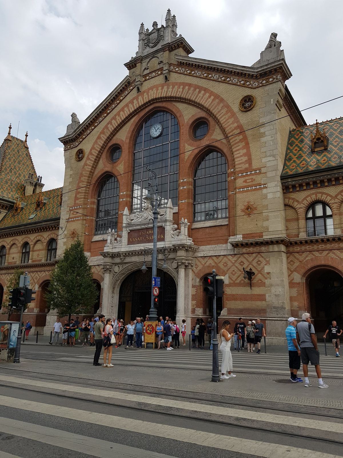 The brick facade of a market hall with people crossing the street