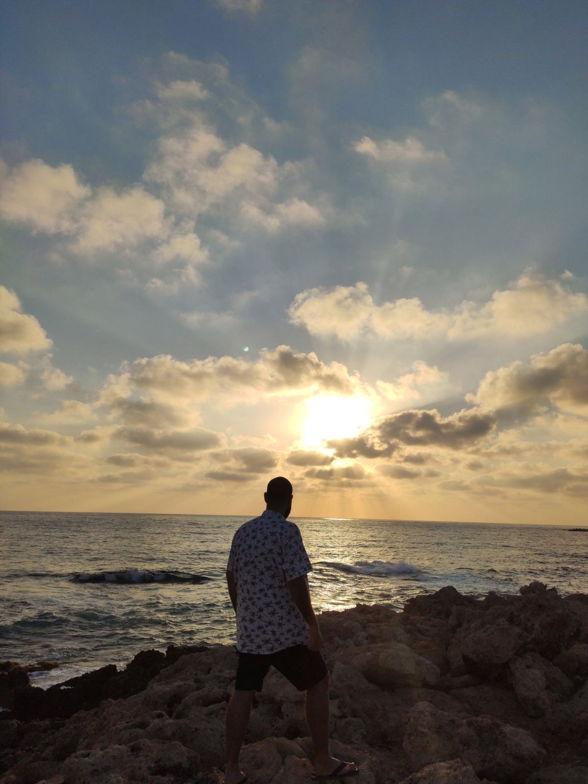 A traveller standing on coastal rocks facing the sunset