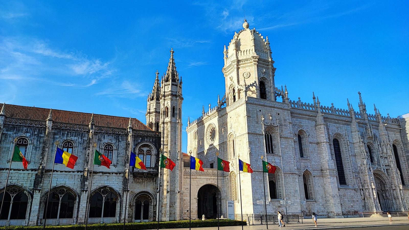 A carved stone monastery facade with flags under a blue sky