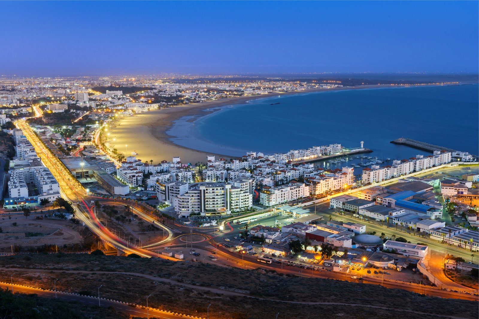 A coastal city and its curved bay lit up at dusk